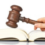 Judge holding a wooden gavel over the law book, reflected on white background Judge holding a wooden gavel over the law book, reflected on white background